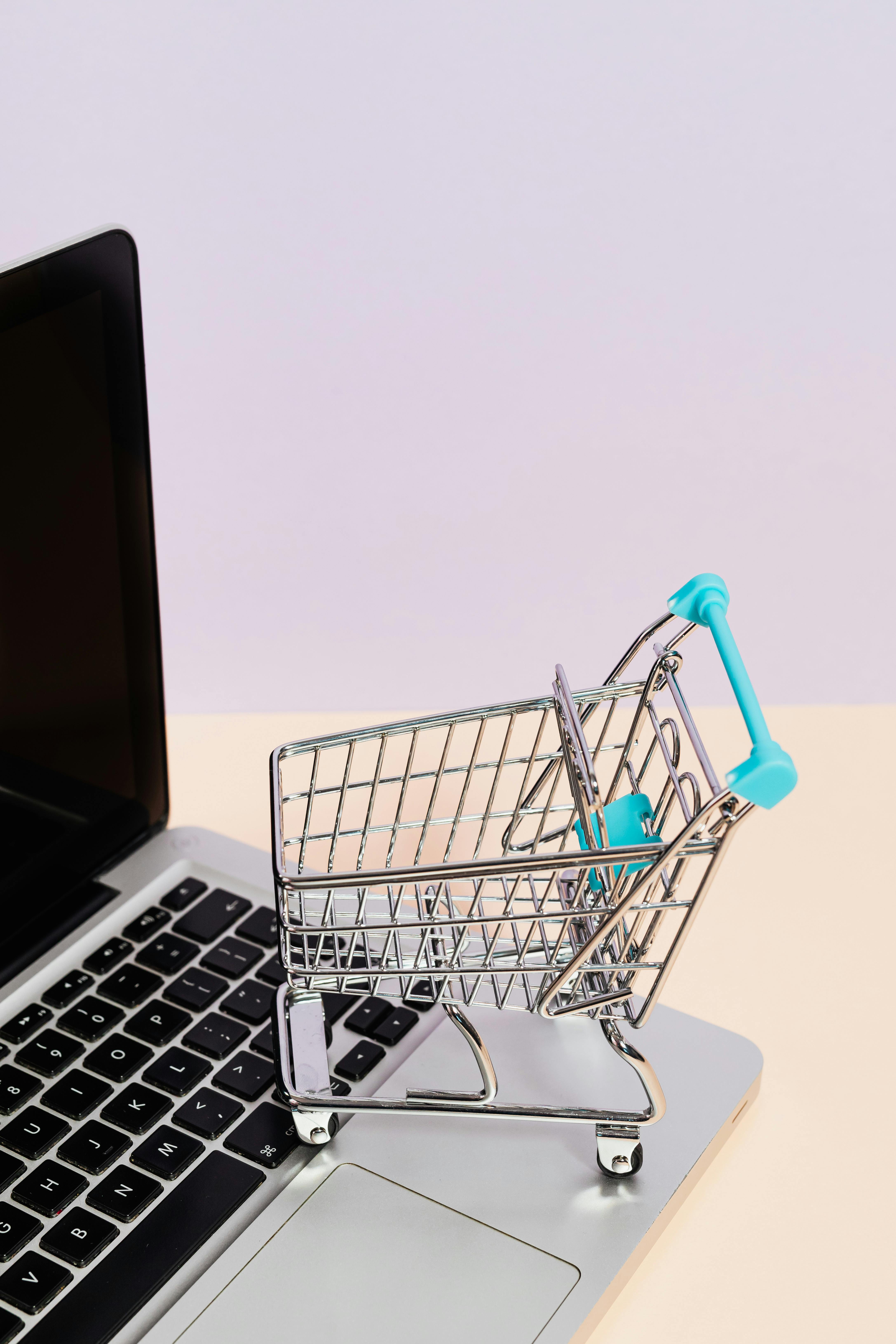 A small miniature of a shopping cart sits on the keyboard of an open laptop, symbolizing the start of an electronic consumer journey.